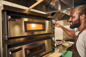 man operating pizza oven in pizzeria