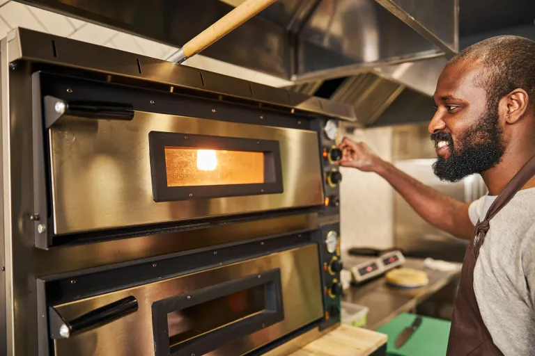 man operating pizza oven in pizzeria