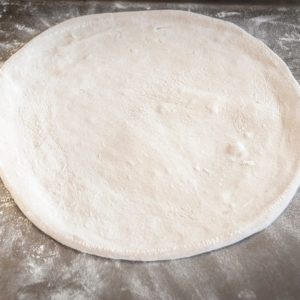 pizza dough stretched out on a wooden board