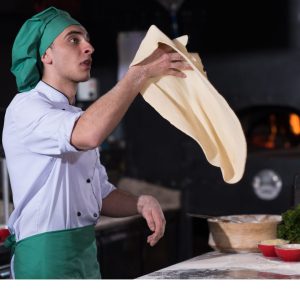 man dressed as a chef in a kitchen tossing and throwing a pizza